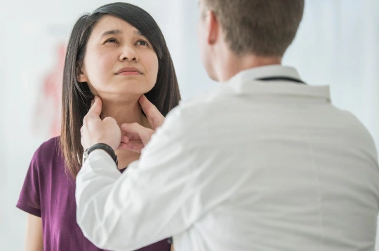 Médecin pratiquant une palpation cervicale sur une patiente pour détecter des ganglions pathologiques.