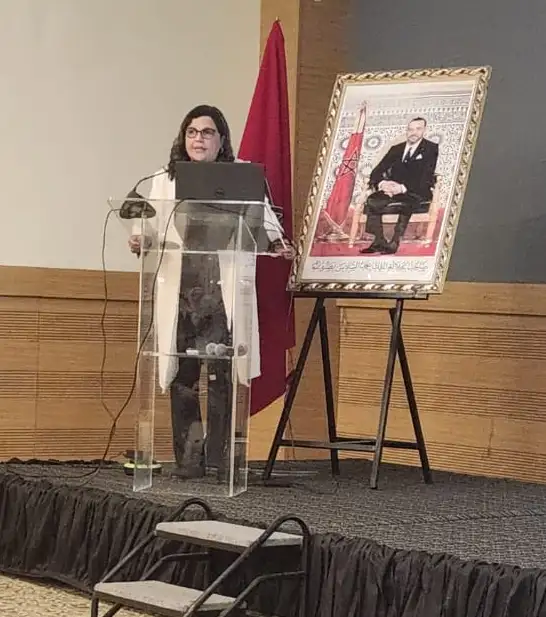 Le Dr. Laila Sabir, pneumologue, fait une présentation lors de la Journée de l'Amicale des ORL de Casablanca, dédiée à la tuberculose ganglionnaire cervicale, avec en arrière-plan le drapeau marocain et un portrait officiel du roi.